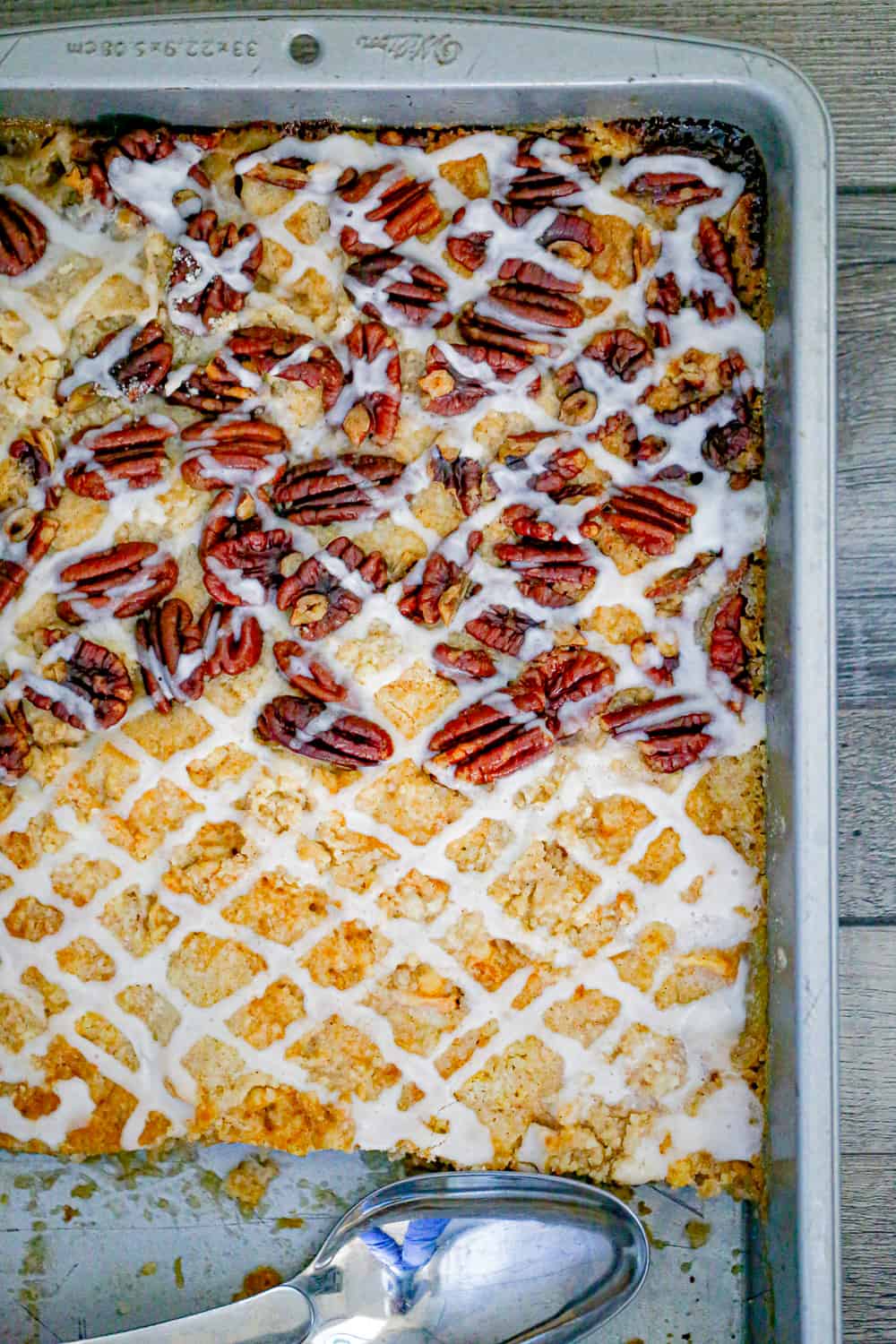 peach dump cake in a pan with peaches, pecans and vanilla glaze