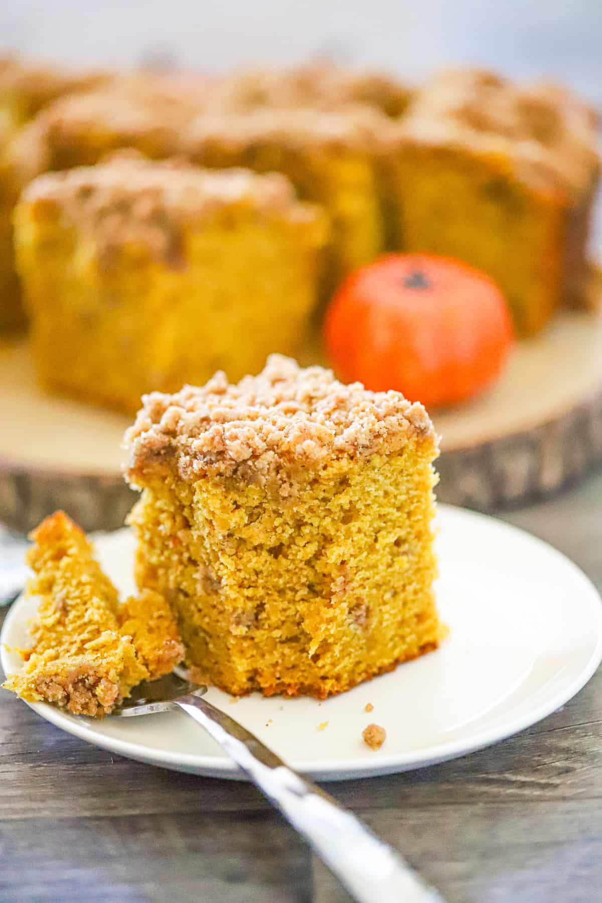 Moist pumpkin crumb cake with crumb topping on white plate with a slice cut out.