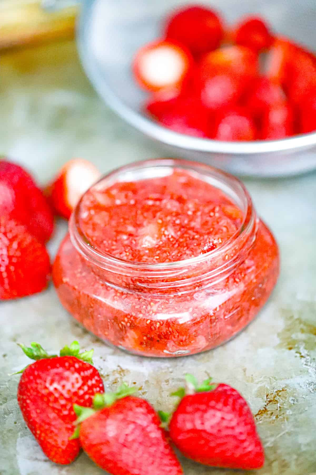 A jar of strawberry jam on a counter with strawberries.
